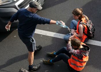 Aktivisten der Letzten Generation bei einer Protestaktion auf der Straße, mit Warnwesten und festgeklebt am Asphalt