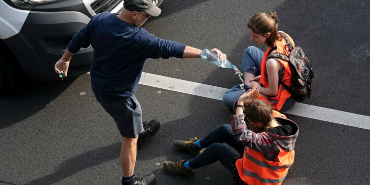 Aktivisten der Letzten Generation bei einer Protestaktion auf der Straße, mit Warnwesten und festgeklebt am Asphalt
