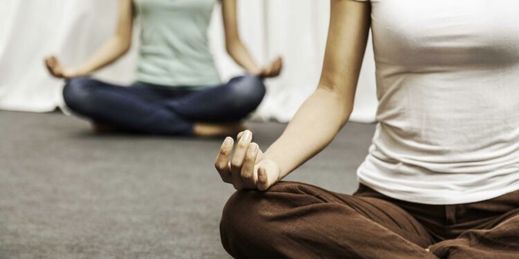 Person meditiert im Lotussitz auf einer hellen Yogamatte, umgeben von sanftem Morgenlicht und natürlicher Atmosphäre