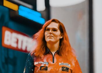 Dartspieler bei einem Turnier, umgeben von Zuschauern und Kameras, die eine kontroverse Situation andeuten