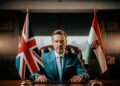 Mann in türkisem Anzug zwischen britischer und ungarischer Flagge – Symbolbild für Norbert Péter und das Hungarian Trading Ho